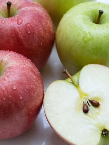 Svježe crvene i zelene jabuke na dasci za rezanje, narezane i cijele, sa sokom od jabuke